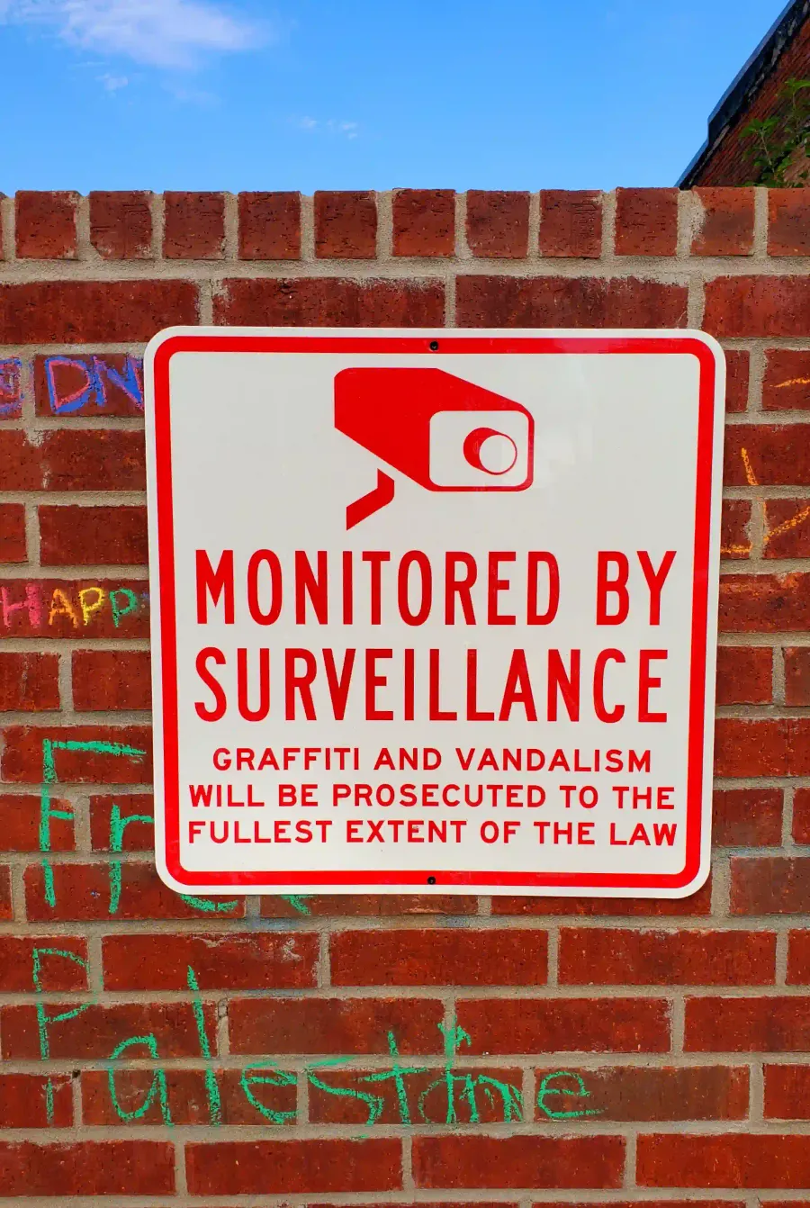 A sign that says, 'MONITORED BY SURVEILANCE' bolted to the graffiti wall