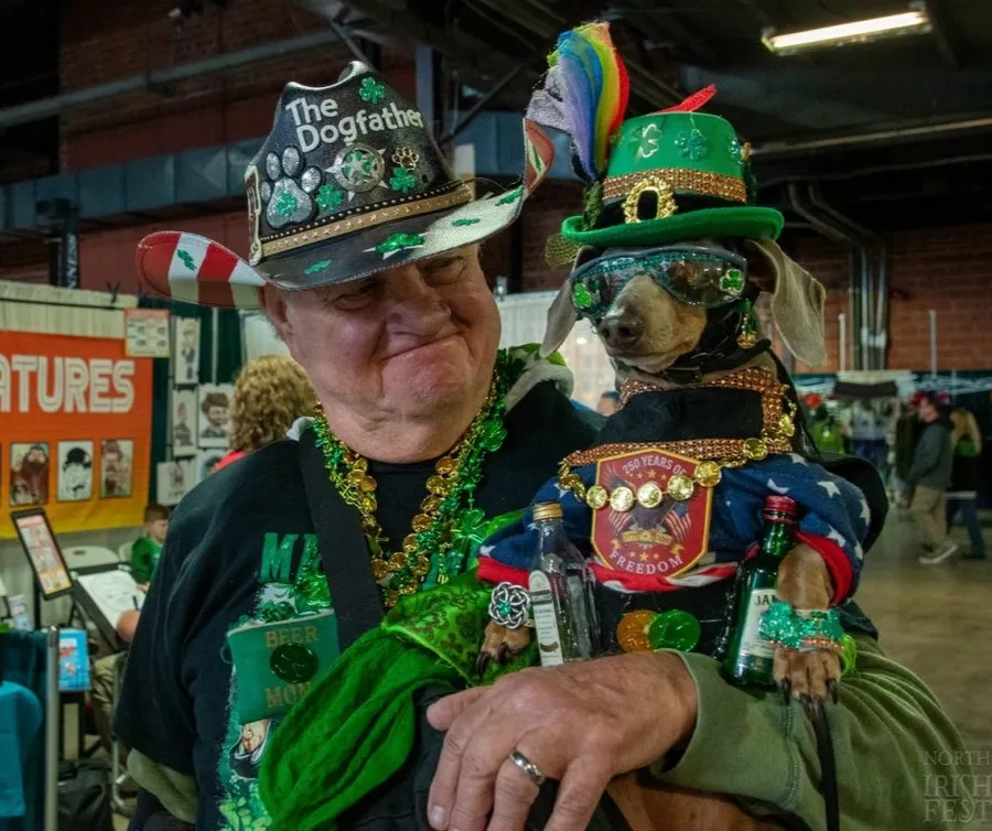 A festival-goer nicknamed 'The Dogfather' holding his dachshund, both dressed head to toe in green St. Patrick's Day gear.