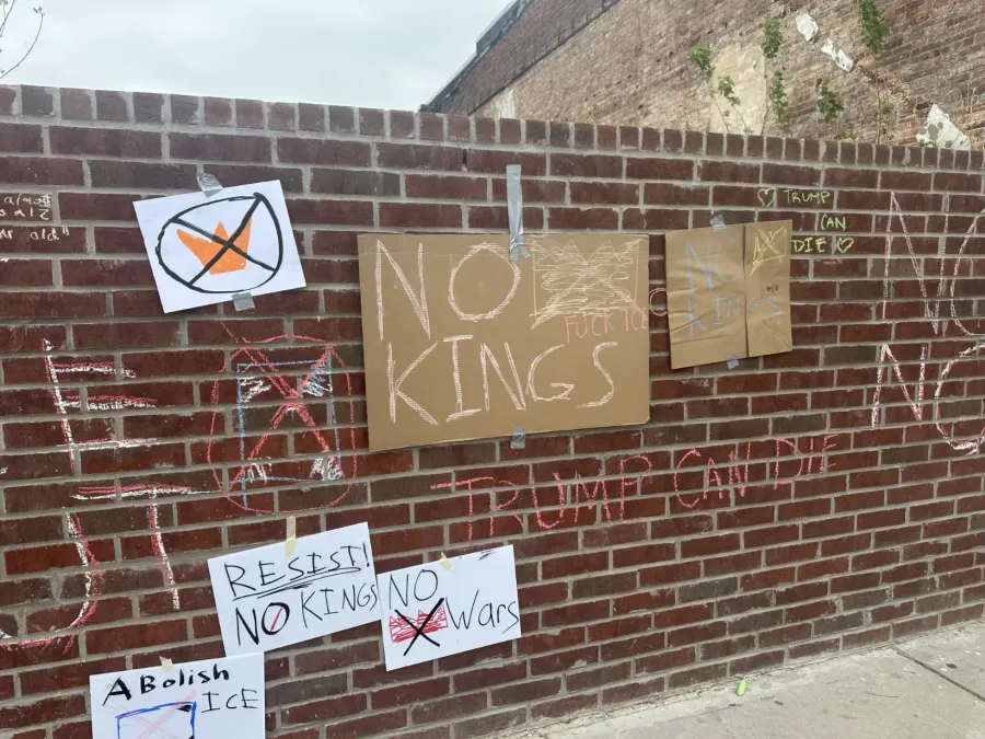 A brick wall covered in chalk messages and handmade signs, with the words 'NO KINGS' and 'DOnald Trump Can Die' written on it