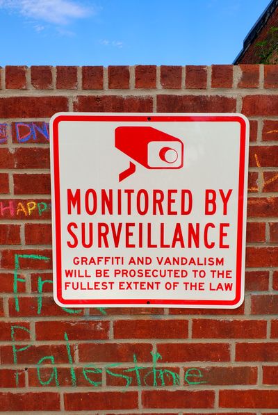 A sign that says, 'MONITORED BY SURVEILANCE' bolted to the graffiti wall
